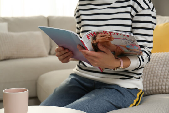Woman reading sports magazine at home, closeup