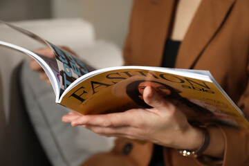 Woman reading fashion magazine on sofa at home, closeup