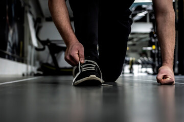 Fototapeta premium Unrecognizable man tying shoelace on sneakers, preparing for daily training. Shot of a unrecognizable man tying his shoelaces while exercising. Man crouching down and tying shoelaces before workout.