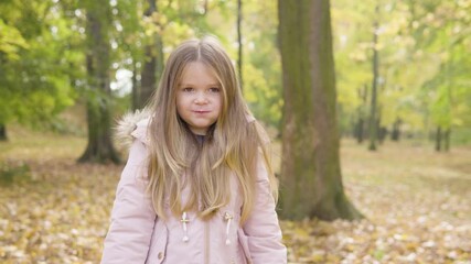 Cute little Caucasian girl eats a snack and smiles at the camera in a park