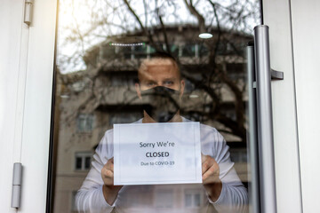 Man with protective face mask closing business activity due to covid-19 emergency lockdown quarantine. Man with protective face mask at fitness center entrance holding closing sign due to coronavirus.