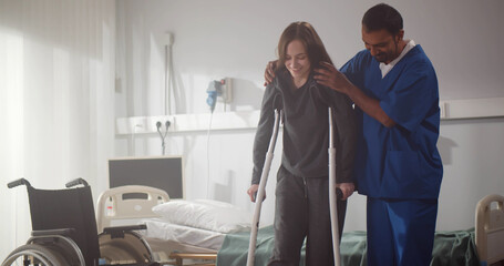 Indian doctor taking care of young female patient in crutch at hospital.