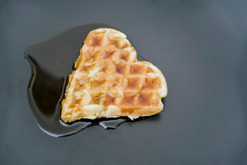 waffle shaped like a heart, with syrup on a black plate