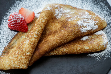 crepe strawberry with powdered sugar on a black plate
