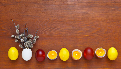Easter bright background for holiday greetings with painted yellow and red traditional Easter eggs and lit candles in eggshells in a row at bottom and free space for text at the top on wooden backdrop
