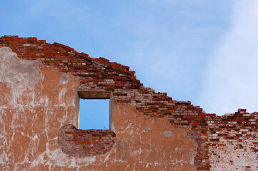 Fototapeta na wymiar Red brick ruins of old building facade with window over blue sky background