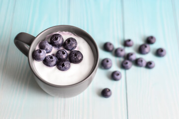 cup with yogurt and blueberries on background of blue boards. Delicious milk yogurt and scattered berries on wooden table top. healthy diet food. Space for text. View from above. Flat lay.
