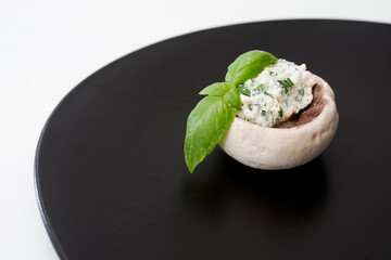 Raw champignon mushroom with cream cheese and mediteranian herbs on a black ceramic plate