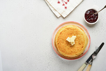 Crepes or thin pancakes stack with butter and raspberry jam on beautiful ceramic plate on an old gray concrete background. Top view, copy space. Homemade thin crepes for breakfast or dessert.
