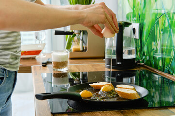 Close up view of of hands breaking egg and making scrambled eggs with toasts on frying pan