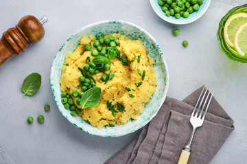 Mashed potato with butter, green peas, onions, basil in a white bowl on a light slate, stone or concrete background. Top view with close up.