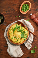 Mashed potato with butter, green peas, onions, basil on a rustic wooden background. Top view with close up.