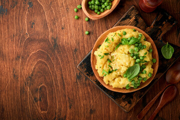 Mashed potato with butter, green peas, onions, basil on a rustic wooden background. Top view with close up.