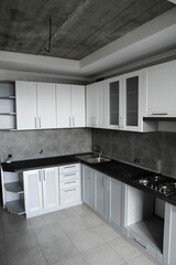 Modern minimalism style kitchen interior in monochrome tones. Custom kitchen with grey white facadesmdf and dark grey countertop with installed kitchen hood and sink. Modular kitchen from chipboard.
