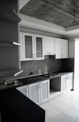 Modern minimalism style kitchen interior in monochrome tones. Custom kitchen with grey white facadesmdf and dark grey countertop with installed kitchen hood and sink. Modular kitchen from chipboard.