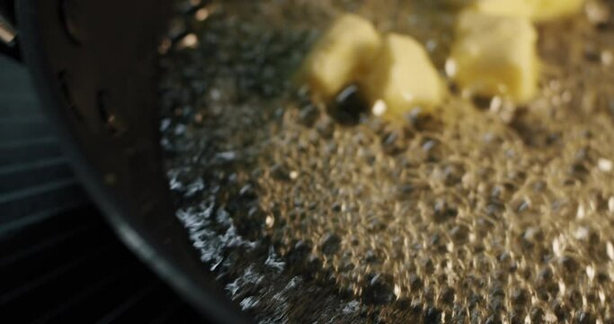 Big pies of butter is added to a hot frying pan with tablespoon and the butter melts and squirts in slow motion (100@25fps)