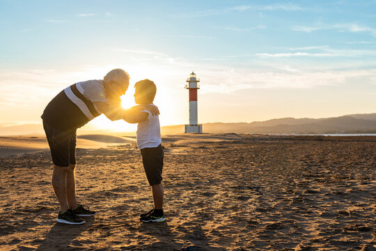 Grandfather and grandson hugging on a beach with a lighthouse in the background