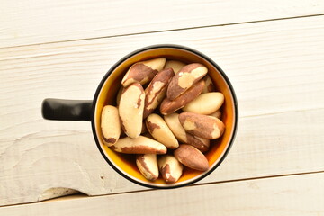 Several delicious organic Brazil nuts with a ceramic cup on a wooden table, close-up, top view.
