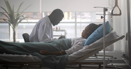 African male doctor checking up female patient in hospital ward