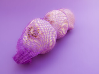 Garlic in net. Garlic packaging nets. Three garlic heads packaged in a mesh bag. Fresh garlic head wrapped in mesh bag