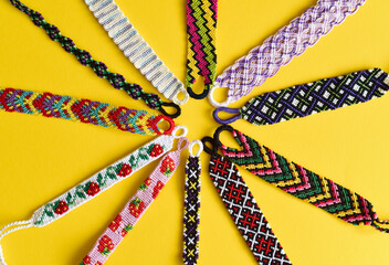 Woven DIY friendship bracelets handmade of embroidery bright thread with knots isolated on yellow background.