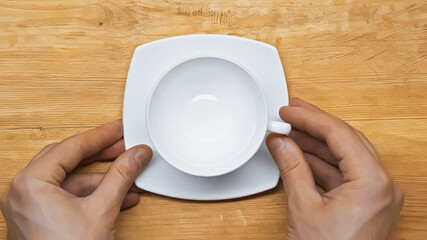 cropped view of male hands near white, empty cup and saucer on wooden table