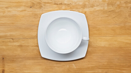top view of white, empty cup and saucer on wooden surface