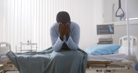 Portrait of afro-american sick patient sitting on hospital bed and rubbing face