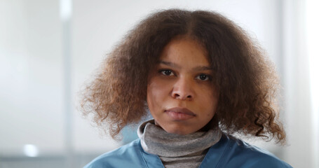 Portrait of young tired afro-american female doctor looking at camera in hospital corridor