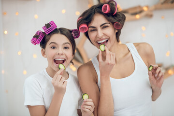 Cheerful naughty mom and daughter with cucumber slices