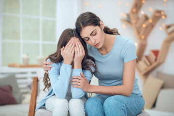 Fototapeta premium Mom hugging daughter covering face with hands