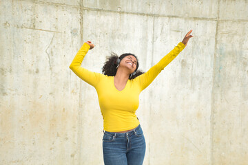 African american woman with afro hair and yellow t-shirt and bluetooth headphones dancing happily.