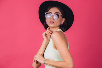 Beautiful stylish woman in hat and sunglasses posing over pink red background, isolated copy space