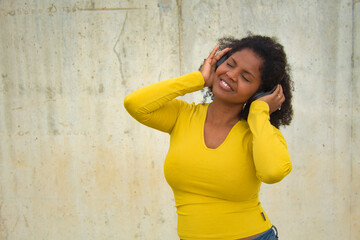 African american woman with afro hair and yellow t-shirt and bluetooth headphones dancing happily.
