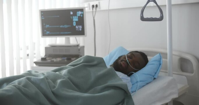 Portrait of afro-american man in coma dying in hospital bed with heart rate falling on ecg monitor