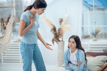 Standing talking mom and sitting naughty daughter