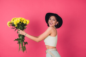 Stylish woman in hat on pink red background sips to left large bouquet of yellow asters, spring...