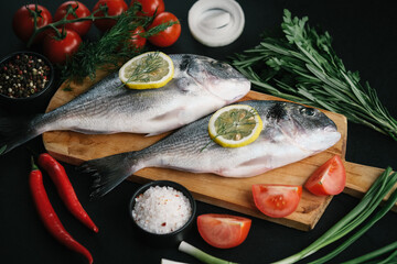 Fresh dorado fish with vegetables and spices on a dark background.
