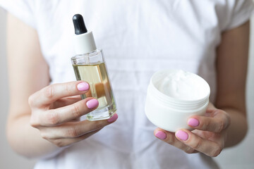 Woman holding skin care products, jar of cream and jar of cosmetic oil in hands