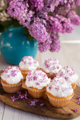 delicious sweet cupcakes decorated with fresh lilac flowers, on a wooden tray, light background,  spring  bouquet of lilacs on the table