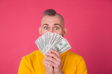 European man on pink red background with fan on 100 dollars shocked excited amazed isolated space