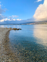 View of the beach with clear water and a large cloud over the mountains