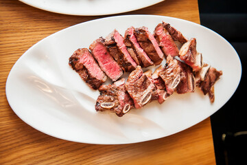 Sliced medium rare steak and ribs on a white plate on the table. View from above. Defocus