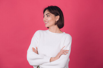 Fototapeta premium Beautiful woman in casual white sweater on pink red background with crossed hands smile look to left isolated copy space