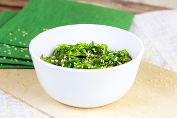 Green Asian seaweed salad in a white bowl on wooden background.