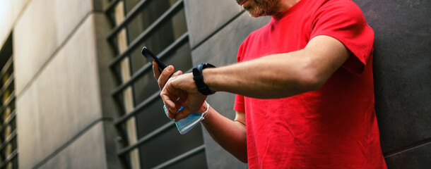 Male using fitness app on smartphone. Man resting after jogging reading run results. Runner with...