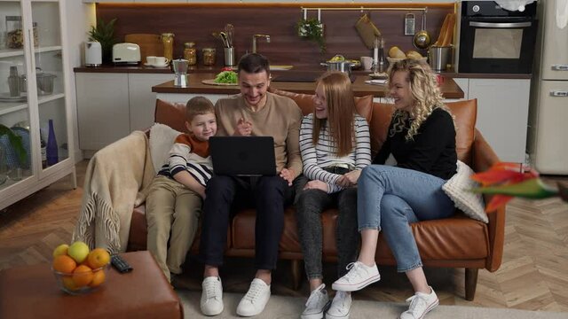 Laughing deaf parents and kids watching amusing video content sitting on sofa at laptop and sharing impressions in sign language. Cheerful people with hearing loss enjoying joint domestic leisure