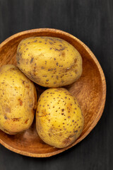 Three boiled potatoes with peels are in a wooden round bowl