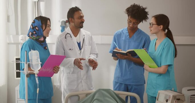 Mature indian doctor giving lecture to interns in hospital ward discussing patient diagnosis