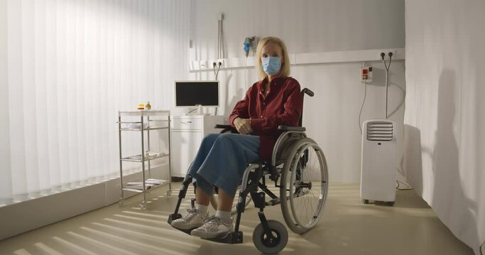 Senior woman patient wearing safety mask sitting in wheelchair at hospital or nursing home